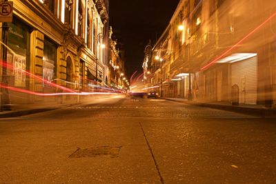 Illuminated light trails on road amidst buildings at night