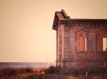 Old building by sea against clear sky during sunset