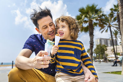 Spain, barcelona, father and son enjoying an ice cream at seaside