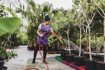 Full length of female owner watering potted plants at nursery