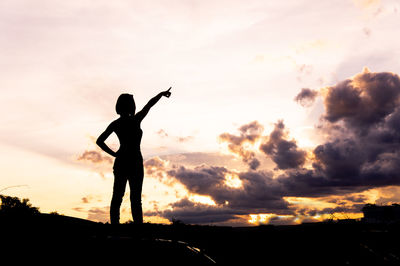 Silhouette woman pointing while standing against sky during sunset