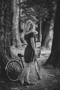 Side view portrait of woman standing with bicycle against trees in forest