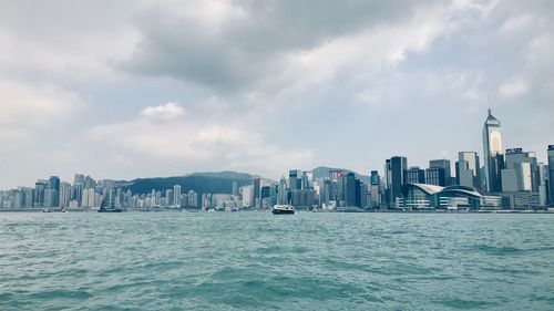 Buildings by sea in city against sky