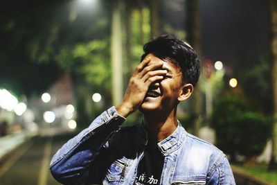 Portrait of young man against illuminated city at night