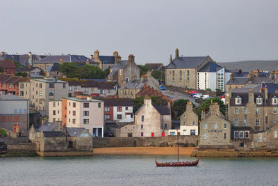 Houses by river against buildings in city against clear sky