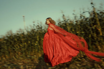 Side view of woman with red dress running against plants