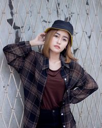 Portrait of beautiful young woman standing against chainlink fence