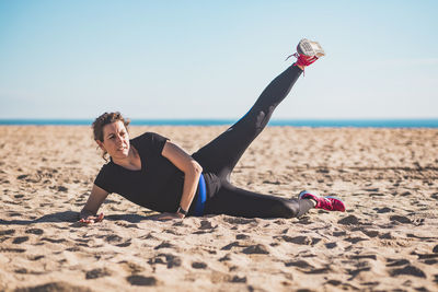 Full length of woman exercising while lying on beach against sky