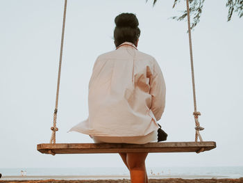 Rear view of man sitting by sea against clear sky