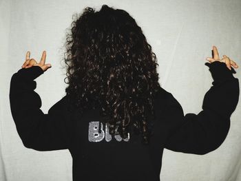 Woman gesturing horn sign while standing against wall