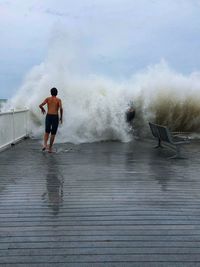 Rear view of man standing in sea against sky