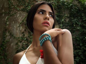 Low angle view of thoughtful woman looking away against creeper plants on wall