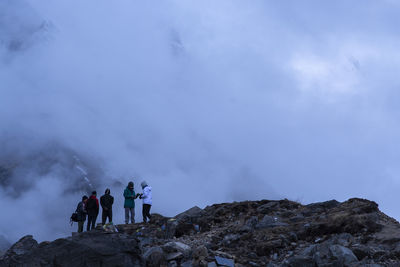 People standing on rock formation against sky during winter