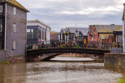 Arch bridge over river amidst buildings against sky