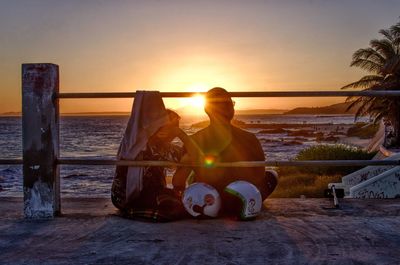 People relaxing on beach against sky during sunset