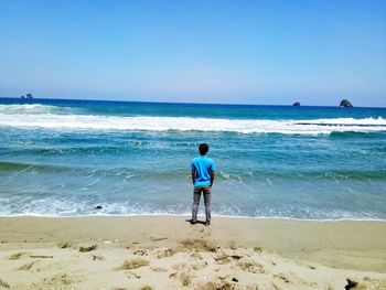 Rear view of man standing at beach against clear blue sky