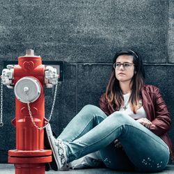 Beautiful woman sitting by fire hydrant against wall