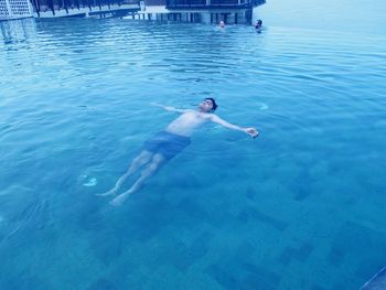 High angle view of carefree shirtless man swimming in infinity pool