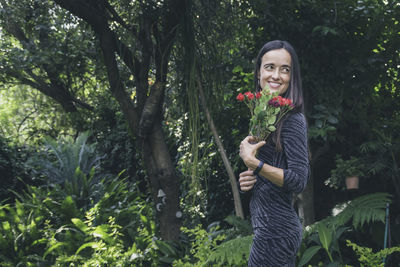 Portrait of smiling young woman standing against plants