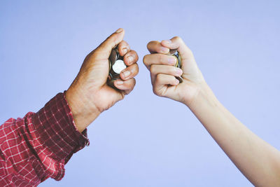 Cropped image of father and son holding coins in clenched fist against purple background