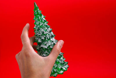 Woman hand holding green christmas tree toy isolated on red background