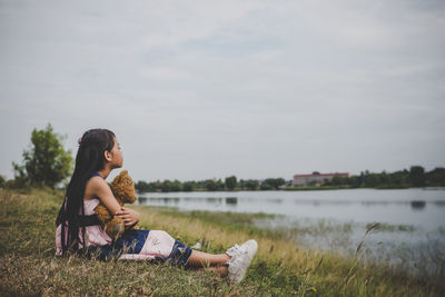Side view of woman relaxing on field against sky