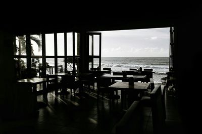 Empty table by sea against sky seen through window