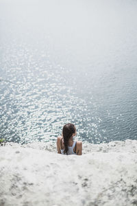 Rear view of woman sitting on cliff in front of sea