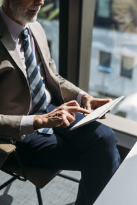 Businessman with tablet pc sitting on chair by window in office