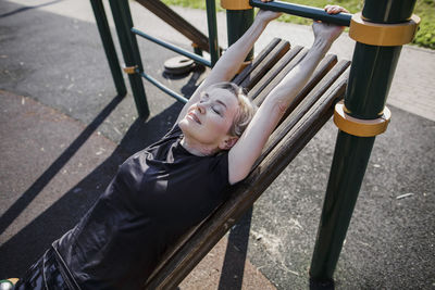 Woman exercising while lying on gym equipment at park