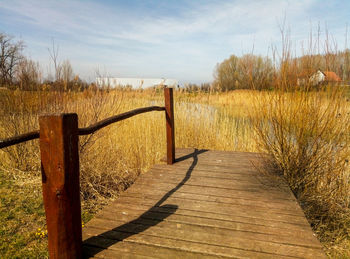 Wooden fence on footpath amidst field against sky