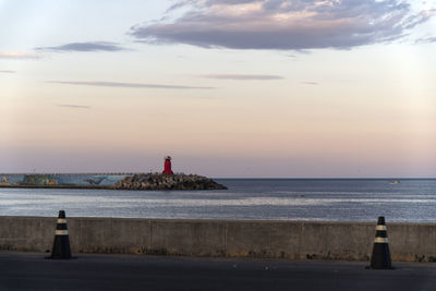 Lighthouse by sea against sky during sunset