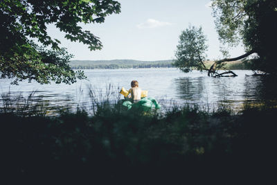 Men sitting by lake against sky