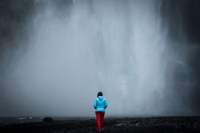 Rear view of woman standing against waterfall during winter