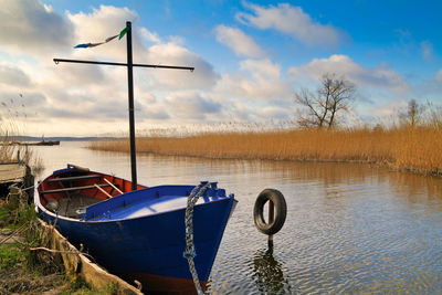 Wide shot of boat moored at lake against cloudy sky