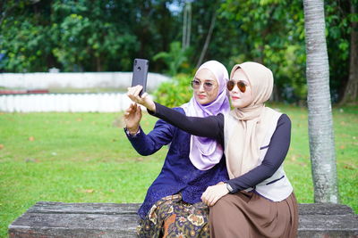 Full length of young woman using phone while sitting outdoors