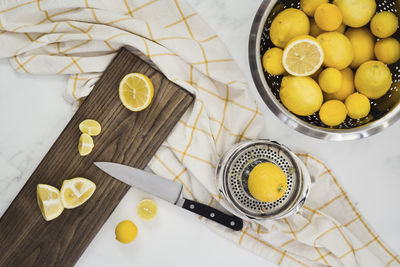 Colander full of whole lemons with cut lemons on board with knife