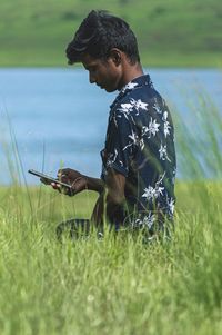 Side view of young man using mobile phone in field