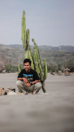 Portrait of smiling man sitting by plant against sky