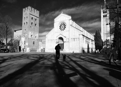 Man with dog walking on street by historic church against sky