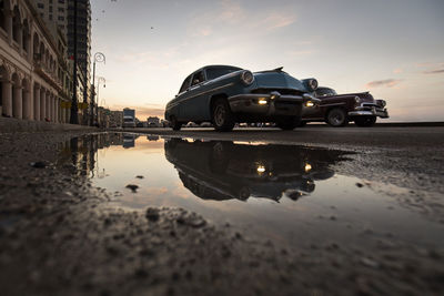 Reflection of building in puddle on road against sky