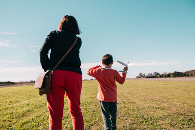 Rear view of friends standing on field against sky