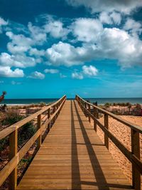 Wooden footbridge leading towards sea against sky