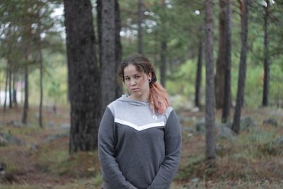 Young woman standing by tree in forest