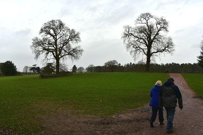 Rear view of people walking on field against sky