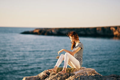 Woman sitting on rock by sea against sky