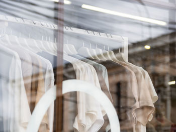 Casual t-shirts hanging on hangers in clothing store. view through transparent shop window.  