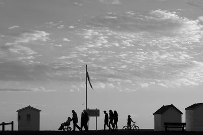 Silhouette people walking on street against cloudy sky