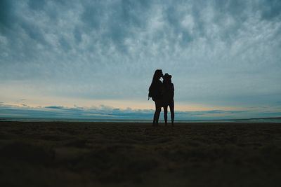 Rear view of silhouette friends standing on sand at beach against sky