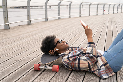 African skater girl chat in smartphone, black female messaging lying on skateboard in skate park